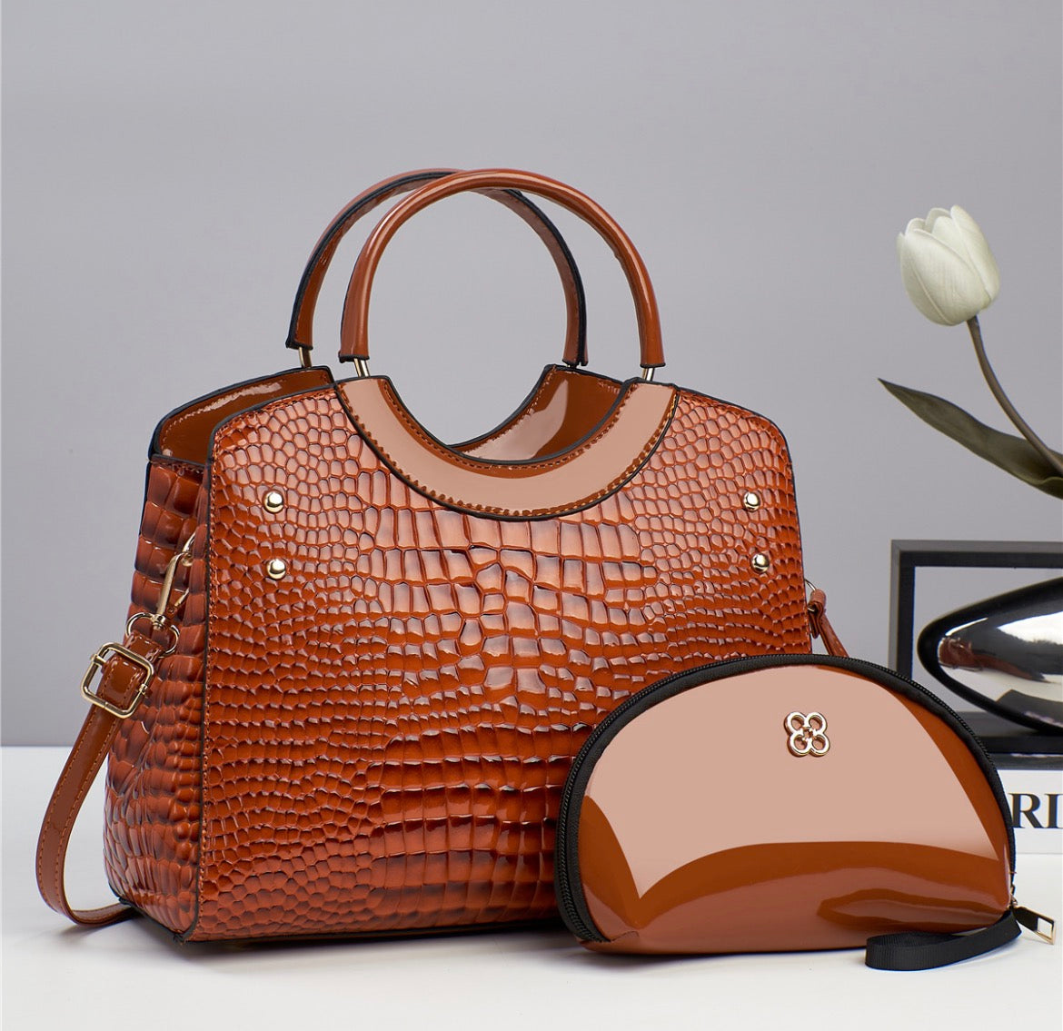 Brown crocodile-style textured handbag with rounded handles and shoulder strap, pictured beside a glossy brown pouch
