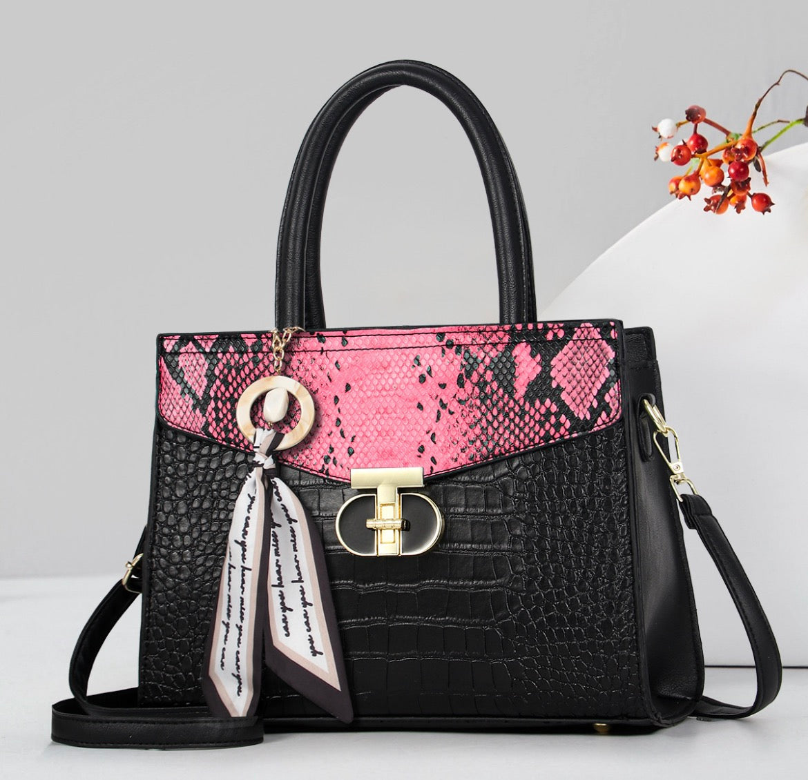 Black textured handbag with pink snakeskin-style flap, gold-tone clasp, scarf accent, and shoulder strap